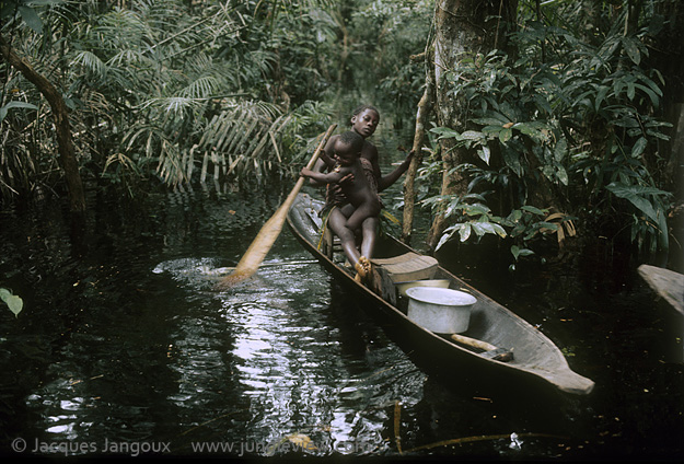 Africa, Democratic Republic of the Congo, Ngiri River islands area, Libinza tribe, girl with baby learning to paddle in canoe in swamp forest.